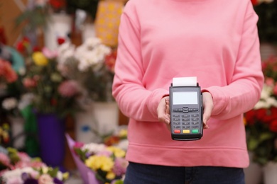 Woman holding payment terminal in floral shop, closeup. Space for text