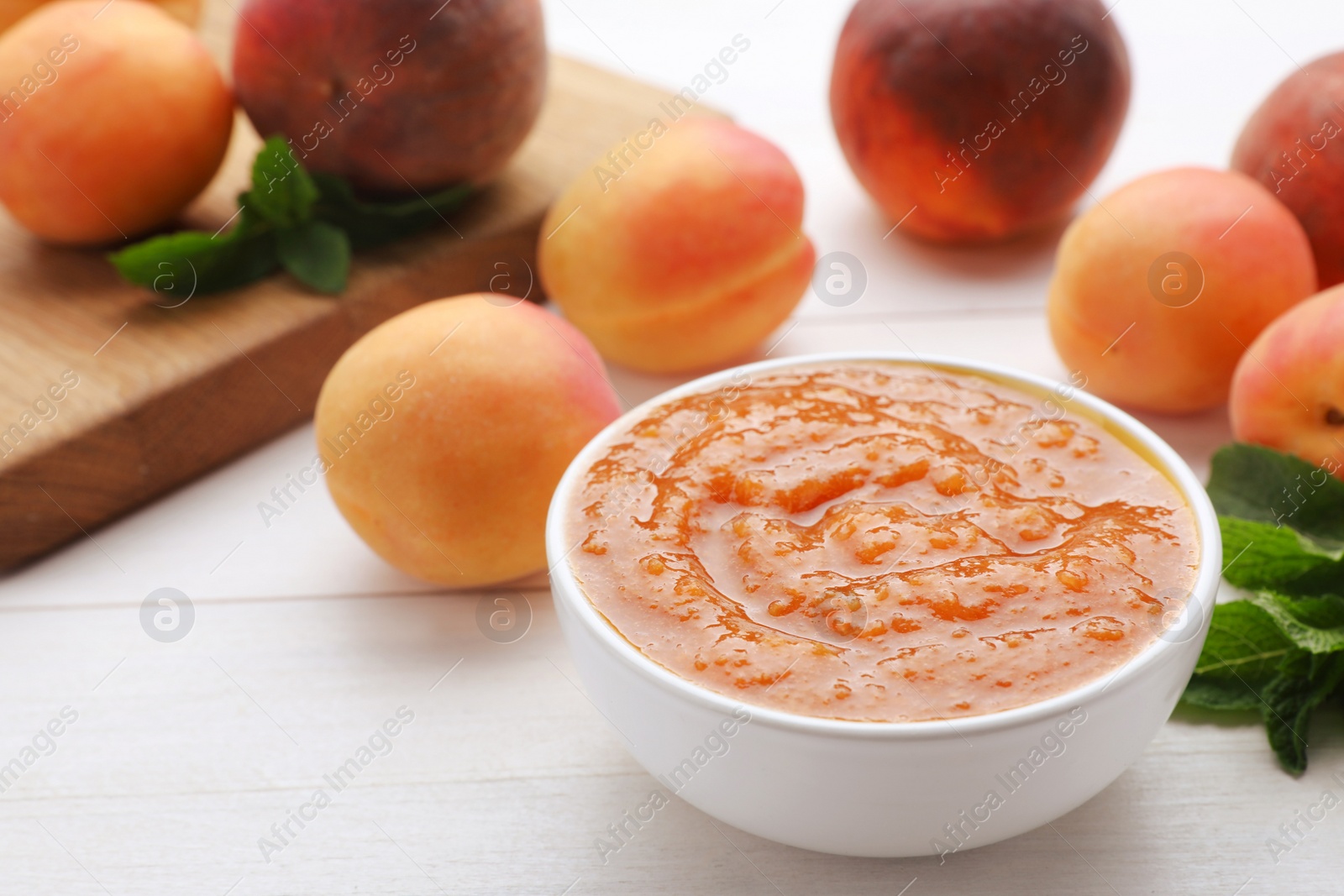 Photo of Apricot puree in bowl and fresh fruits on white wooden table. Space for text