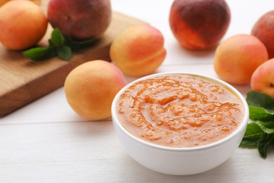 Photo of Apricot puree in bowl and fresh fruits on white wooden table. Space for text