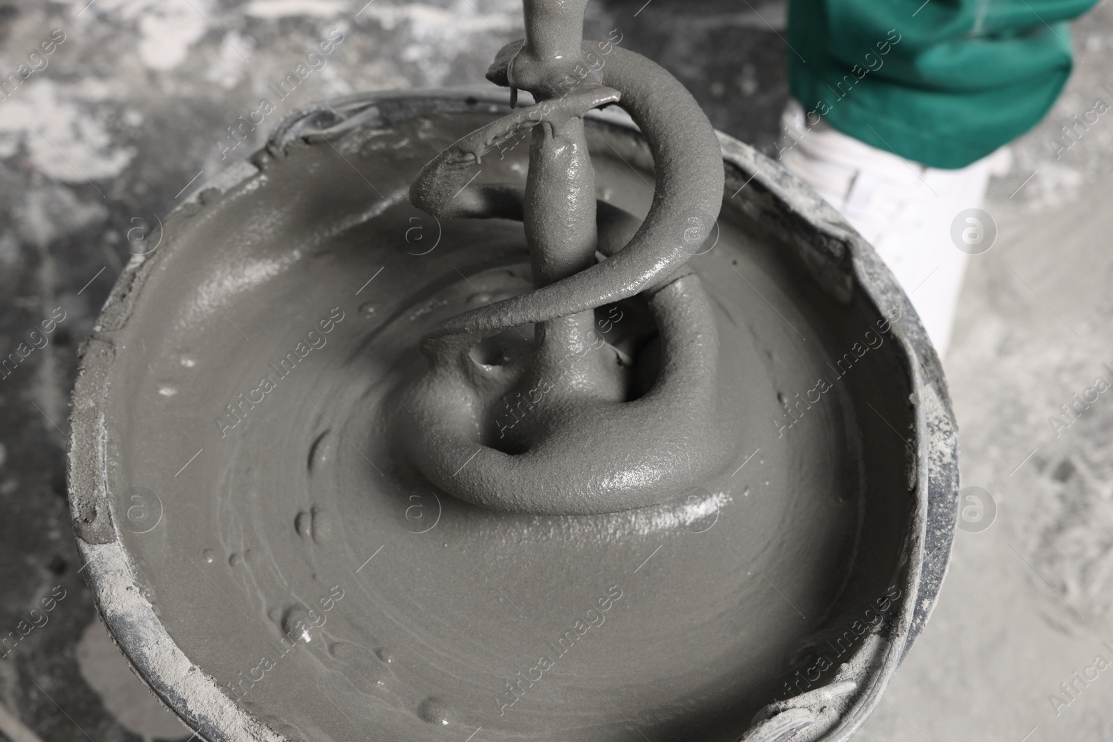 Photo of Worker mixing concrete in bucket indoors, closeup