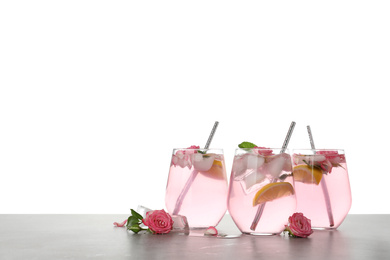 Delicious refreshing drink with rose flowers and lemon slices on light grey table against white background. Space for text