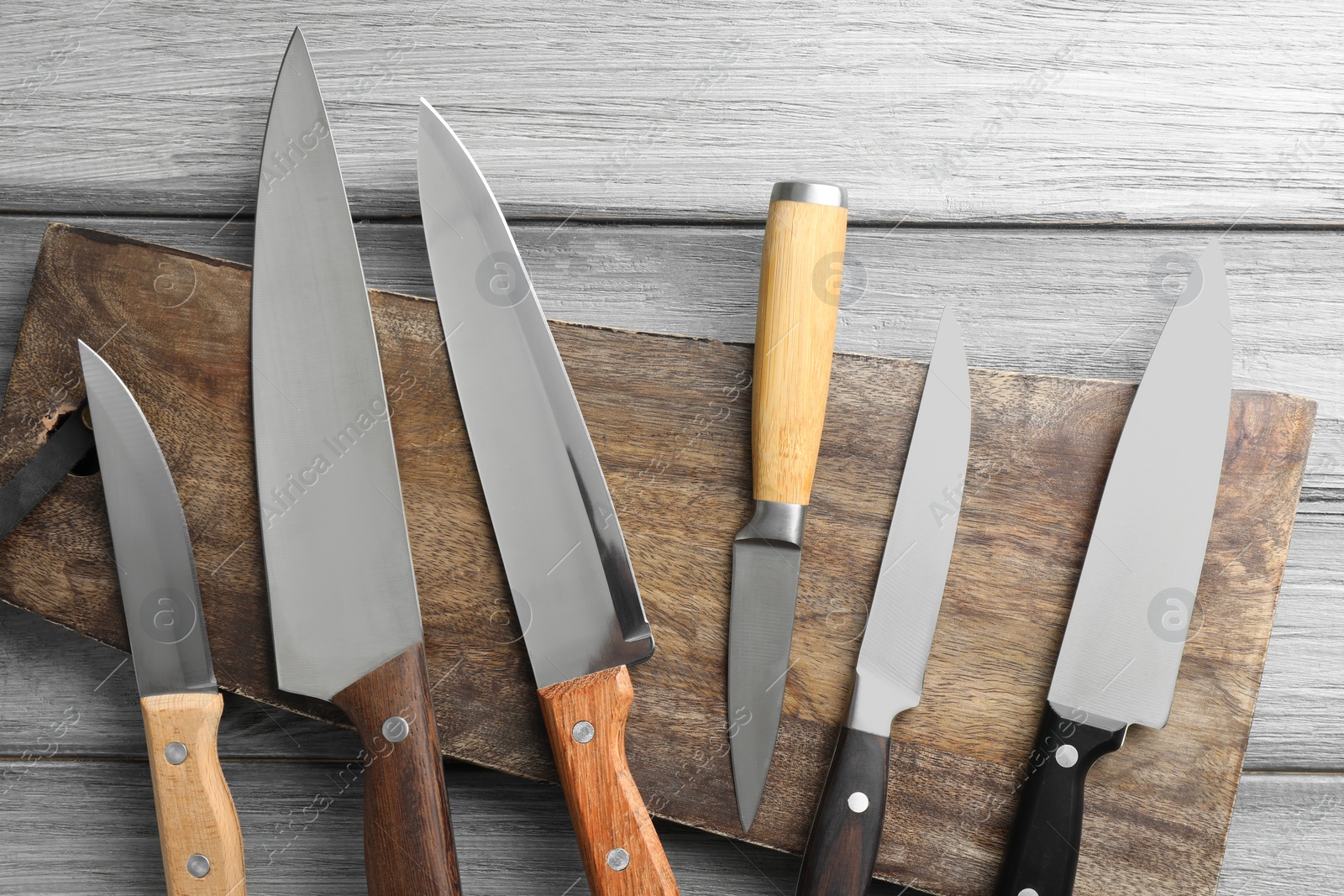 Photo of Many different knives and board on light wooden table, flat lay