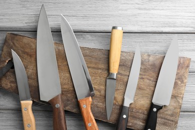 Photo of Many different knives and board on light wooden table, flat lay