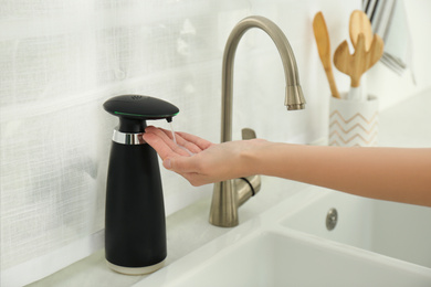 Photo of Woman using automatic soap dispenser in kitchen, closeup