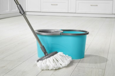 Photo of Mop and bucket on white parquet indoors. Cleaning floor