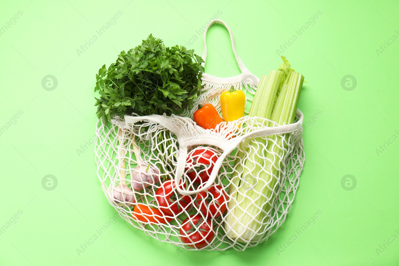 Photo of String bag with different vegetables on light green background, top view