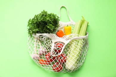 Photo of String bag with different vegetables on light green background, top view