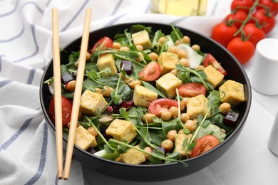 Photo of Bowl of tasty salad with tofu, chickpeas and vegetables on white tiled table, closeup