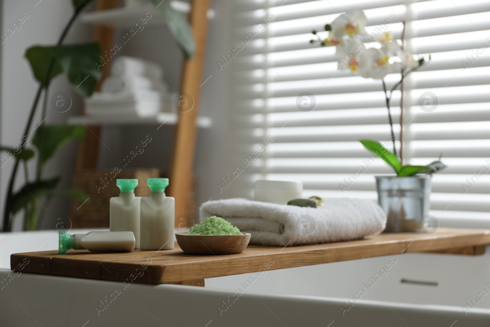Photo of Wooden tray with spa products and orchid flowers on bath tub in bathroom