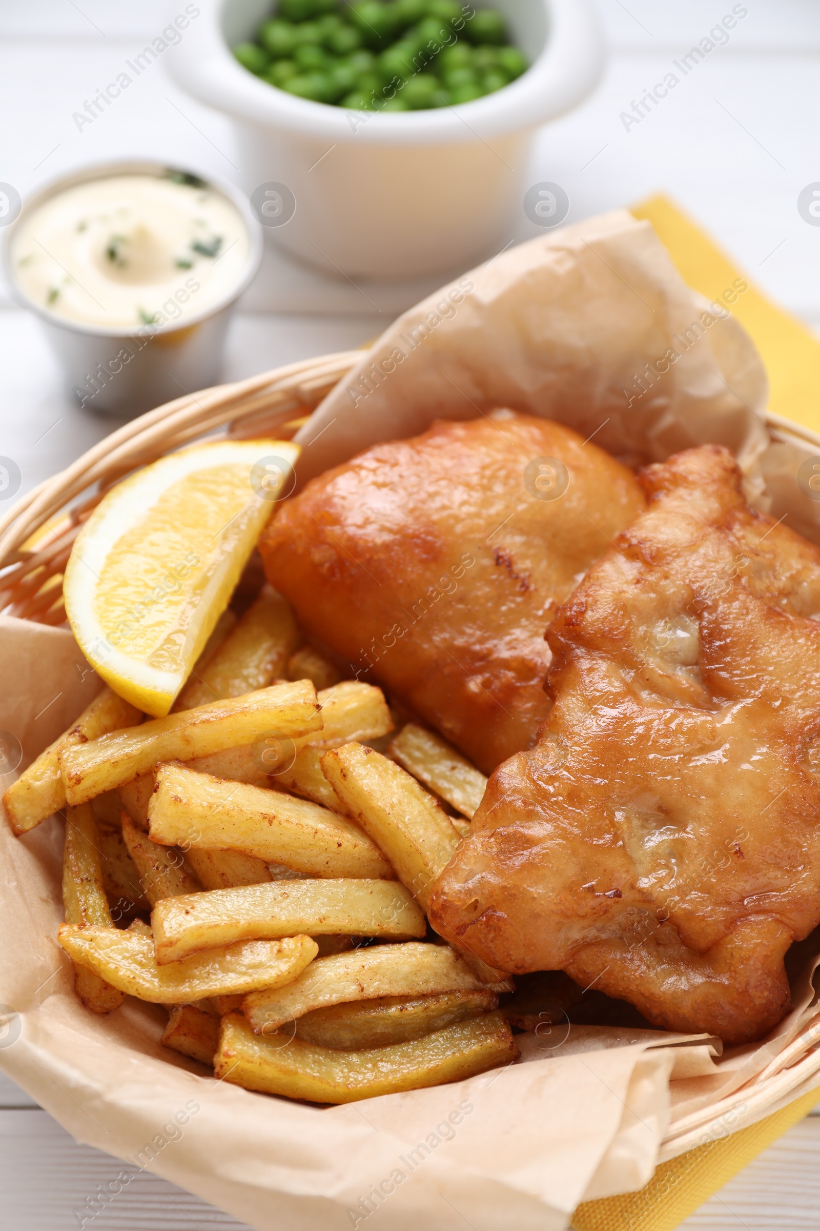 Photo of Tasty fish, chips, sauce and lemon in wicker bowl on table, closeup