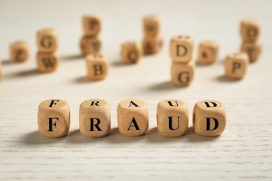 Photo of Word Fraud of cubes with letters on white wooden background. Space for text