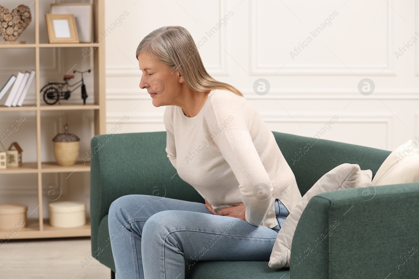 Photo of Menopause. Woman suffering from abdominal pain on sofa at home