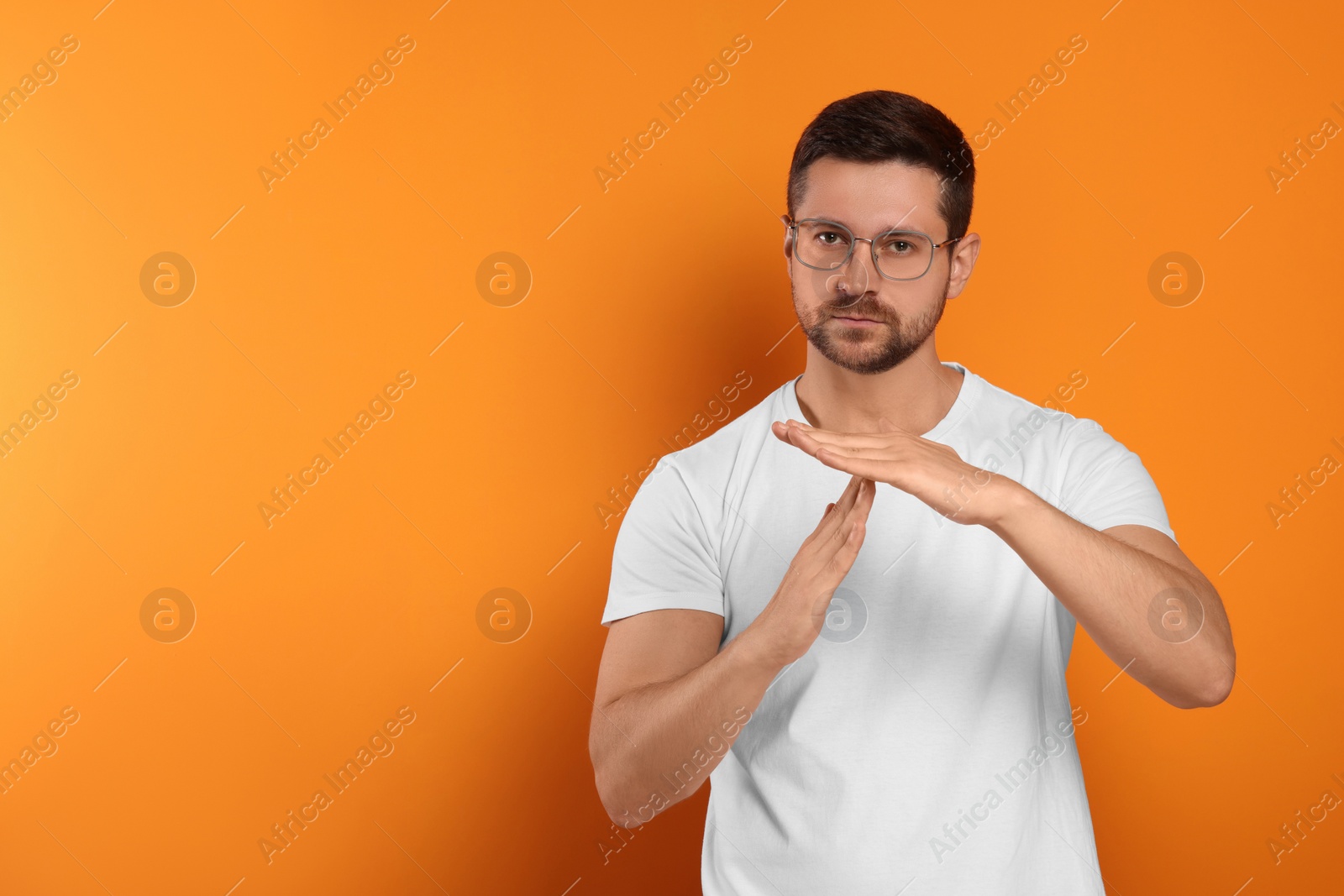 Photo of Handsome man showing time out gesture on orange background, space for text. Stop signal
