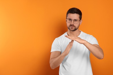 Handsome man showing time out gesture on orange background, space for text. Stop signal