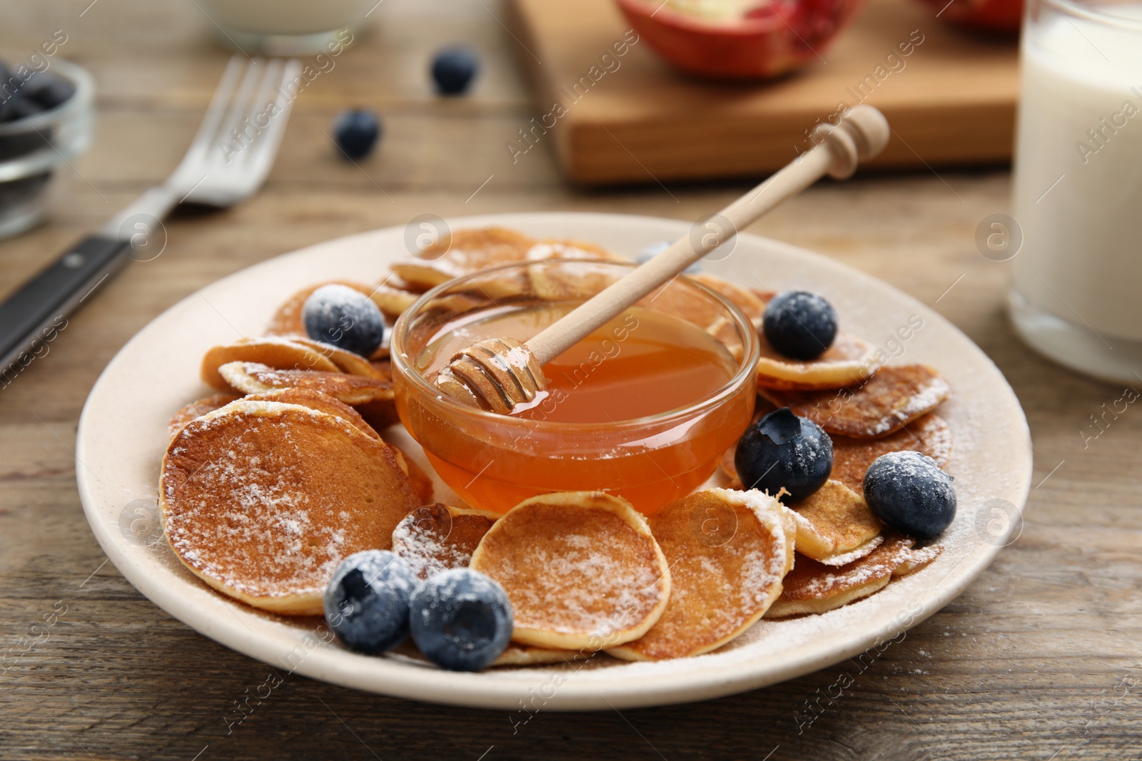 Photo of Delicious mini pancakes cereal with blueberries and honey served on wooden table