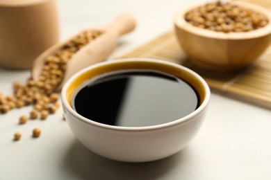 Photo of Soy sauce in bowl and soybeans on white table