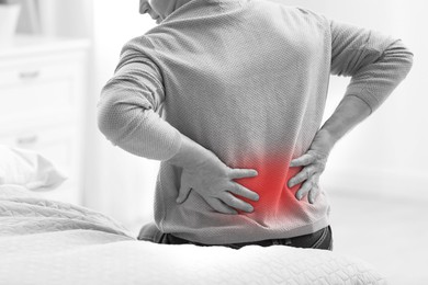 Man suffering from back pain indoors, closeup. Black and white effect with red accent
