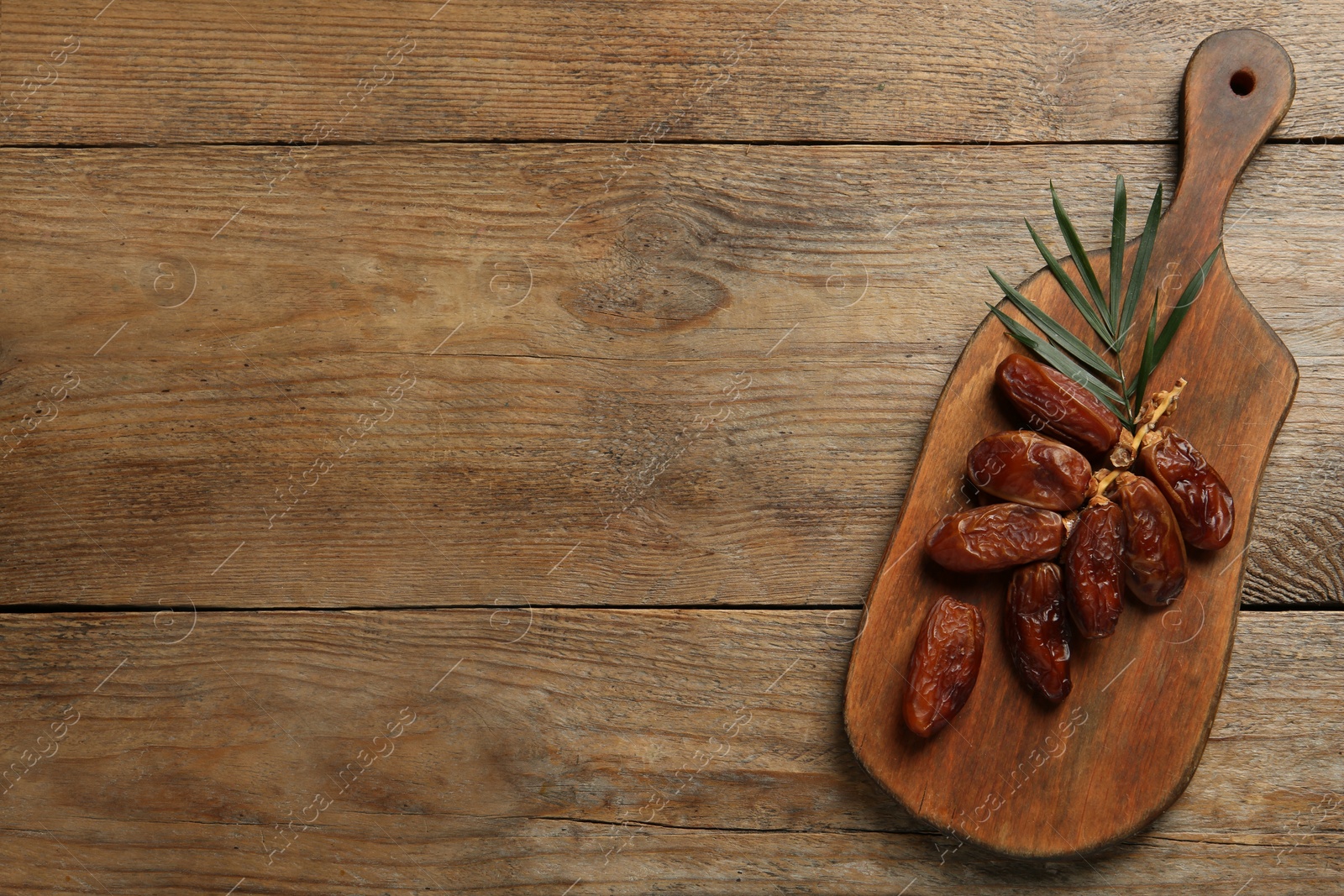 Photo of Sweet dried dates with leaf on wooden table, top view. Space for text