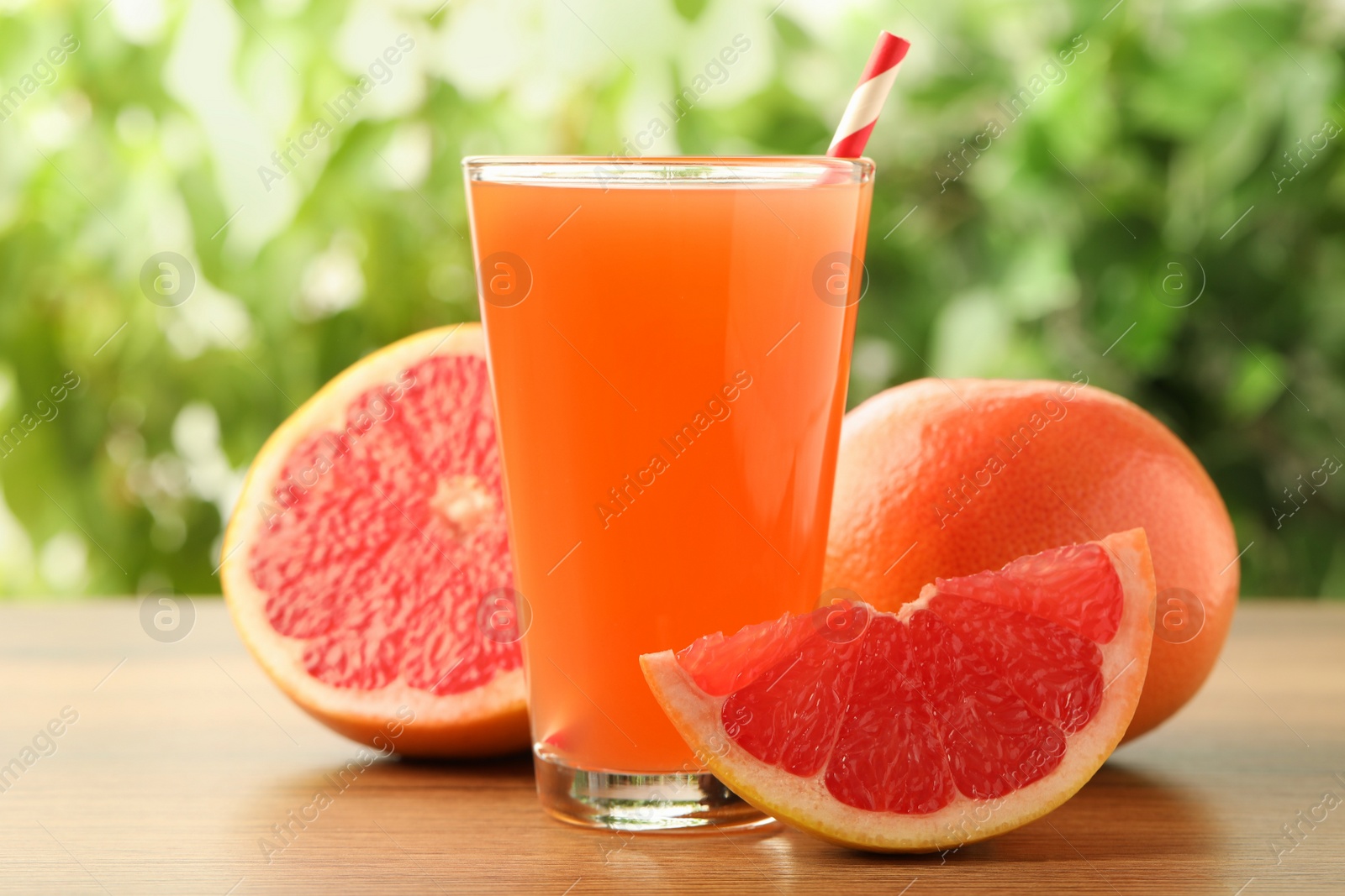 Photo of Glass of delicious grapefruit juice on wooden table against blurred background