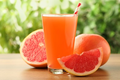 Photo of Glass of delicious grapefruit juice on wooden table against blurred background