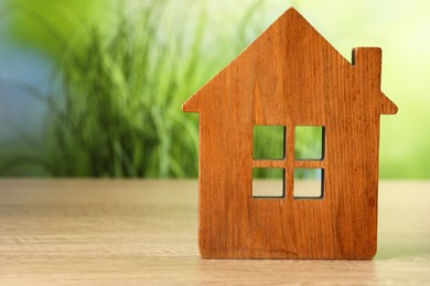 Photo of Mortgage concept. House model on wooden table against blurred green background, space for text