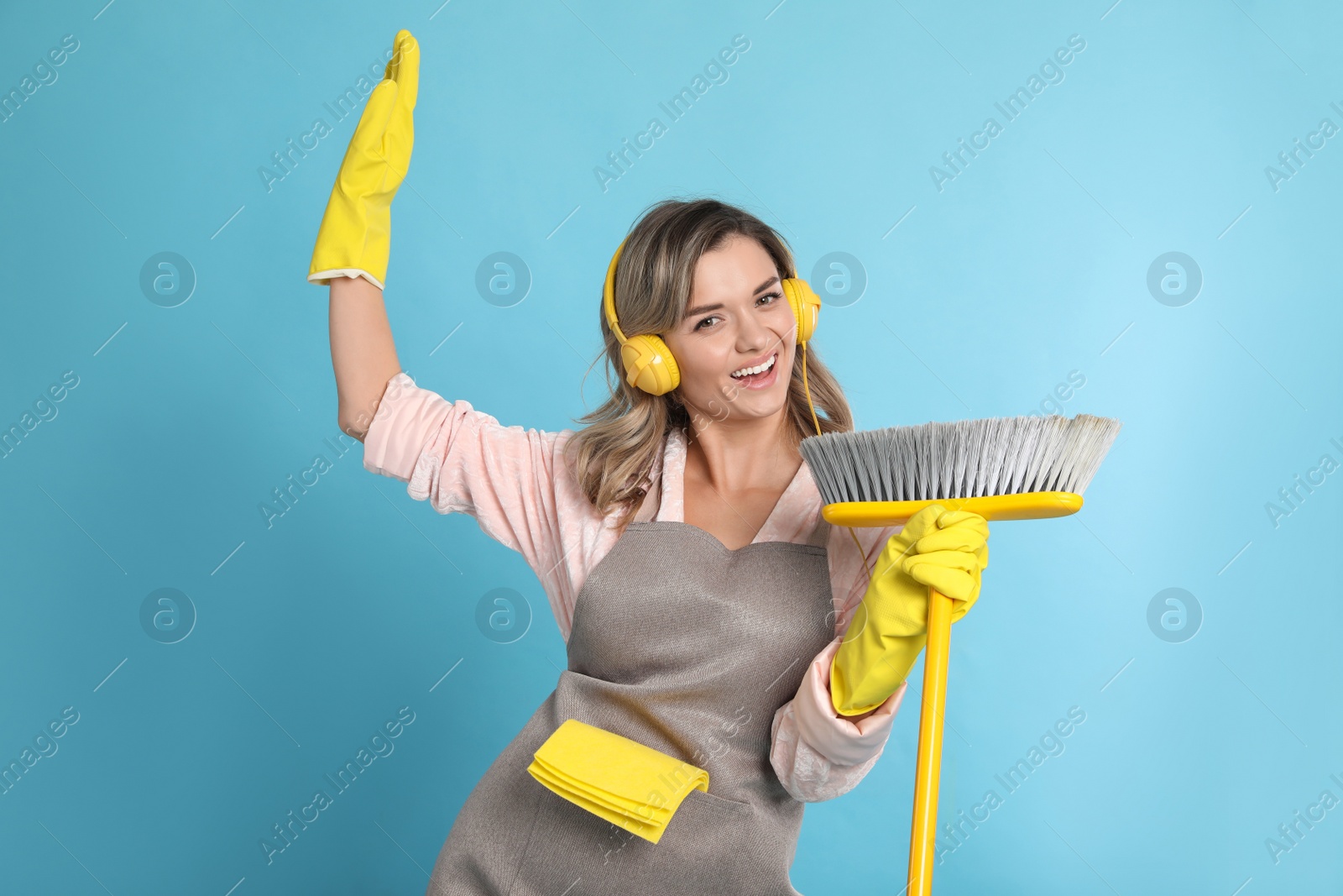 Photo of Beautiful young woman with headphones and floor brush singing on light blue background