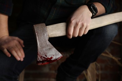 Photo of Man holding bloody axe indoors, closeup view
