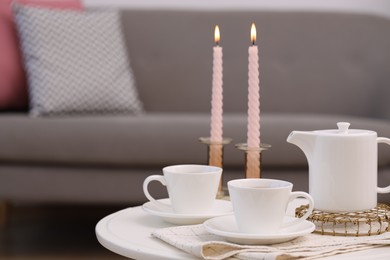 Photo of Cups of tea, teapot and burning candles on white coffee table indoors. Space for text