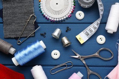Photo of Flat lay composition with thimbles and different sewing tools on blue wooden table