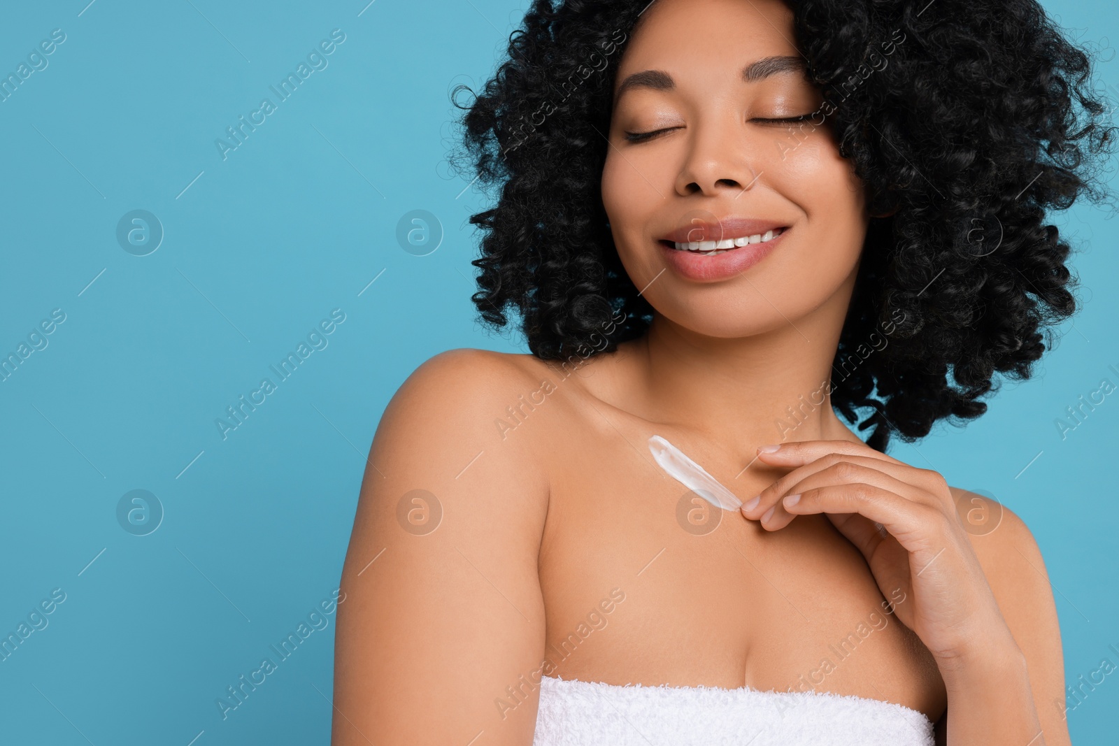 Photo of Young woman applying cream onto body on light blue background. Space for text