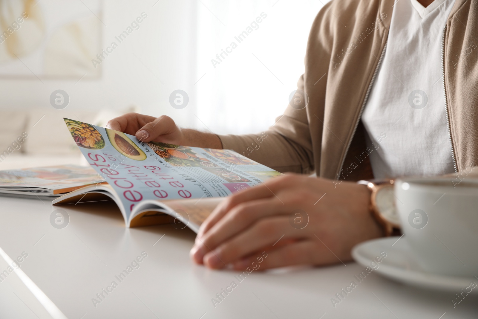 Photo of Man reading culinary magazine at white table indoors, closeup