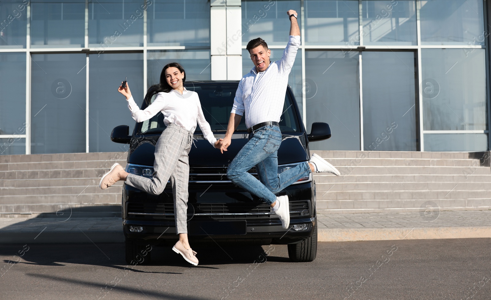 Photo of Excited couple with key jumping near car outdoors. Buying new auto