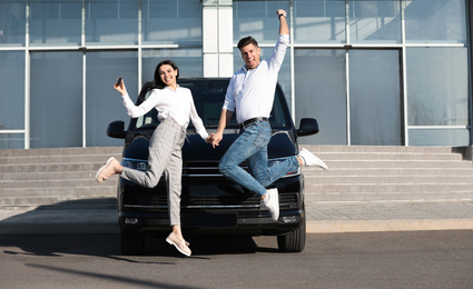 Excited couple with key jumping near car outdoors. Buying new auto