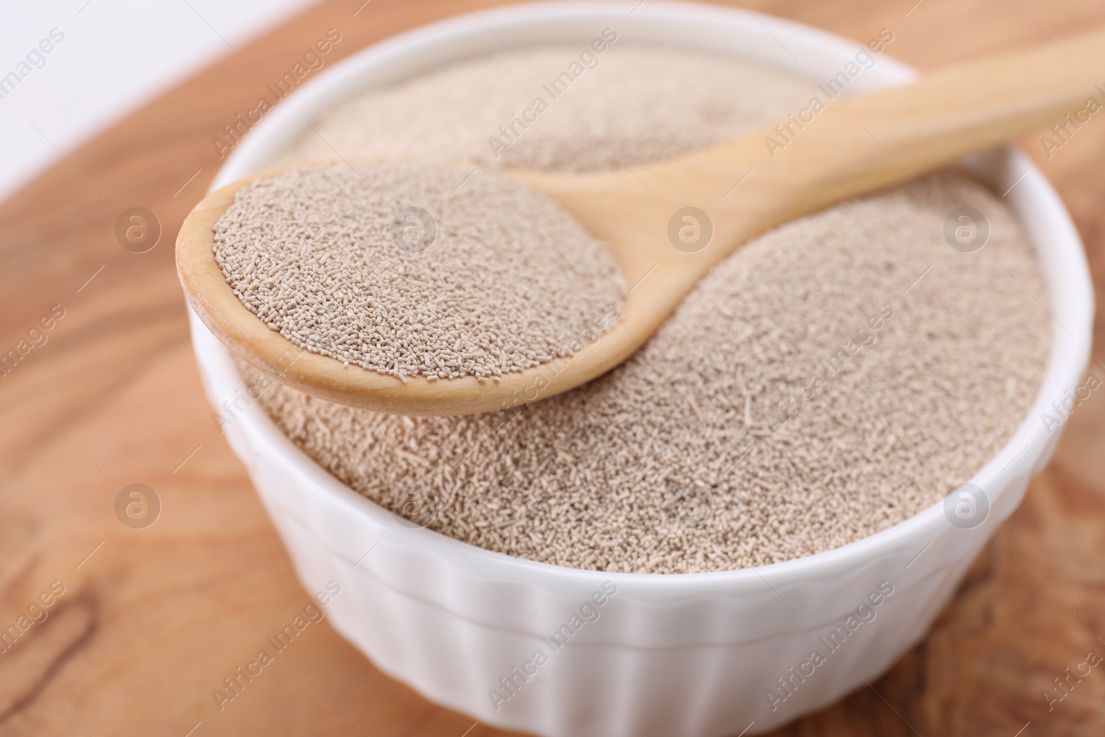 Photo of Bowl and spoon with active dry yeast on wooden board, closeup