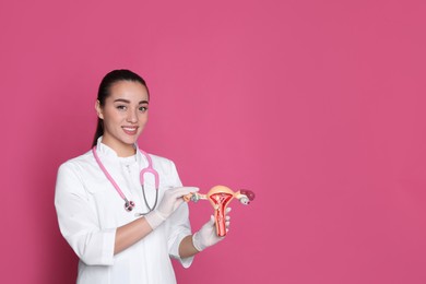 Photo of Doctor demonstrating model of female reproductive system on pink background, space for text. Gynecological care