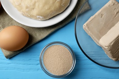 Different types of yeast, egg and dough on light blue wooden table, flat lay