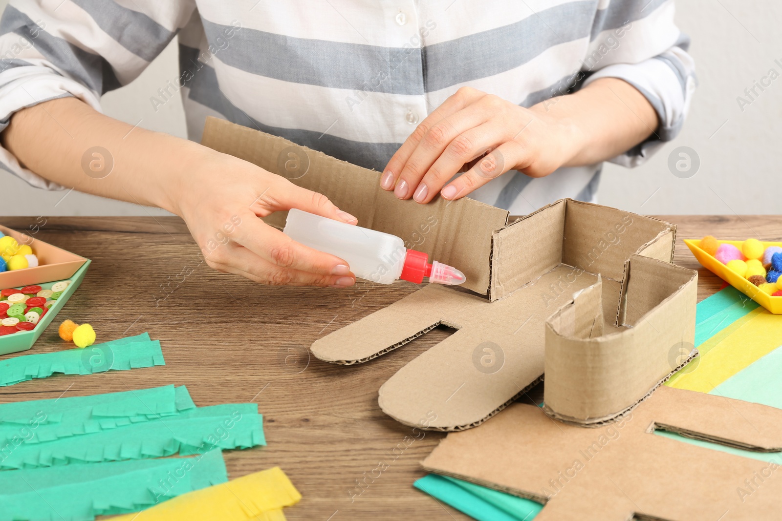 Photo of Woman making cardboard cactus at wooden table, closeup. Pinata DIY