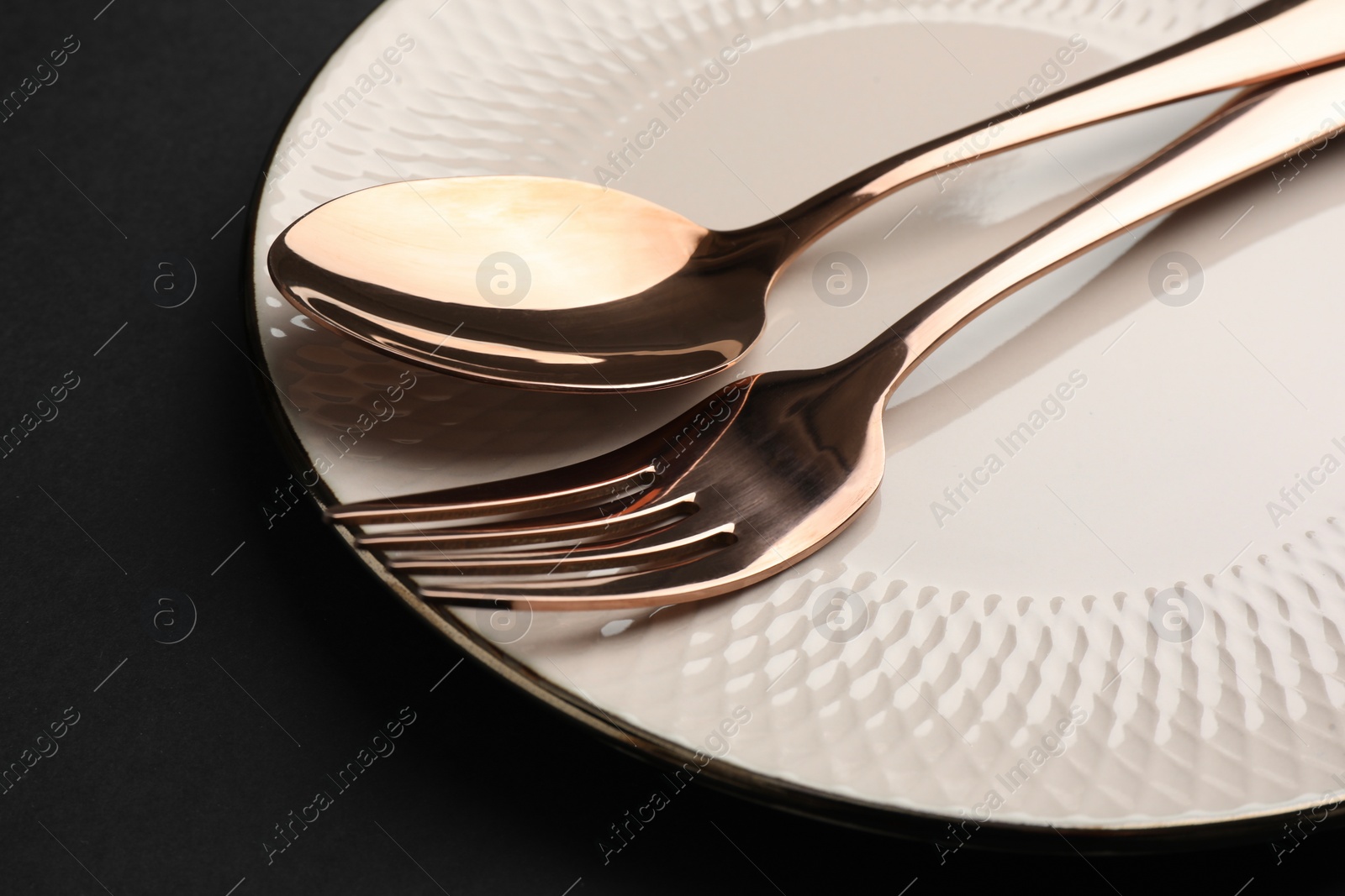 Photo of Clean plate, fork and spoon on black table, closeup