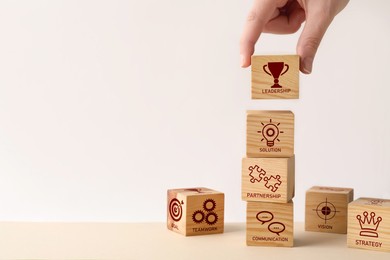 Closeup view of woman stacking wooden cubes with different images at table, space for text. Management concept