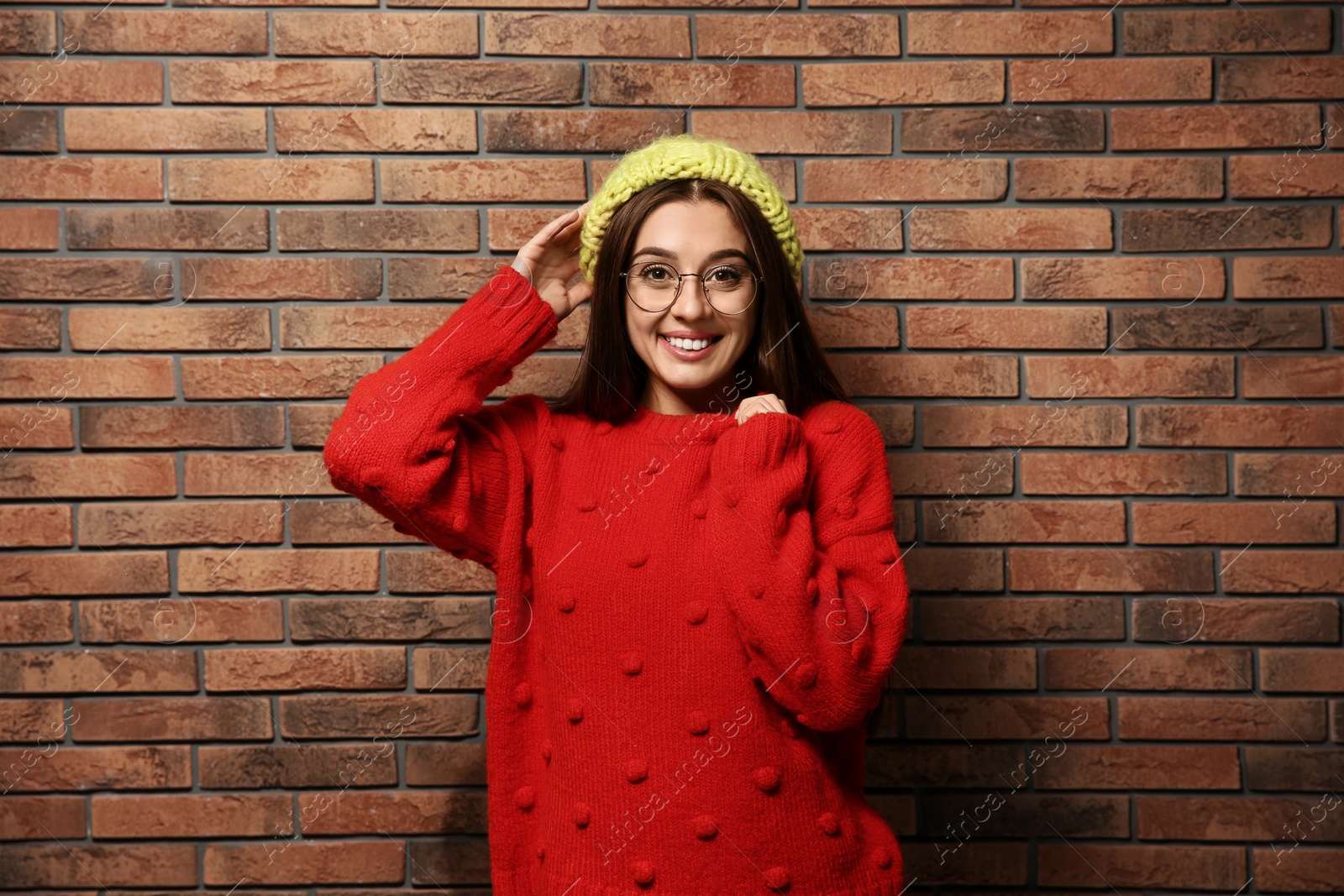 Photo of Beautiful young woman in warm sweater with hat near brick wall