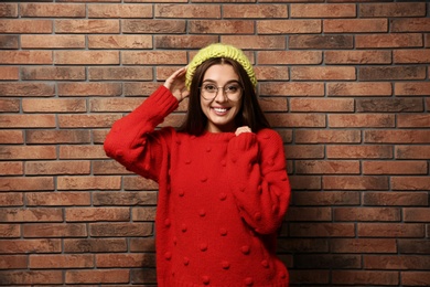 Beautiful young woman in warm sweater with hat near brick wall