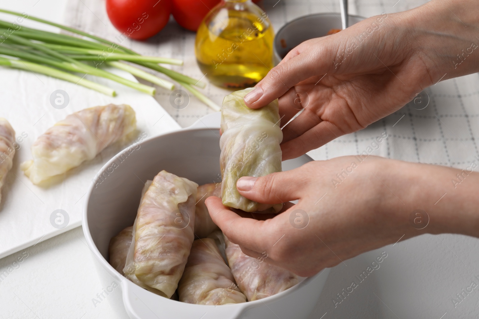 Photo of Woman putting uncooked stuffed cabbage roll into ceramic pot at white table, closeup