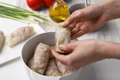 Woman putting uncooked stuffed cabbage roll into ceramic pot at white table, closeup