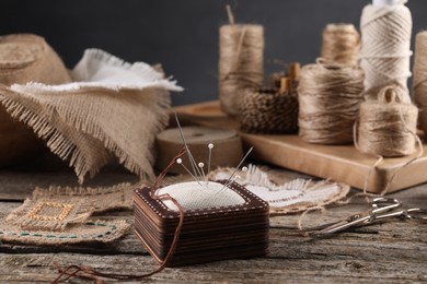 Photo of Pieces of burlap fabric, spools of twine and different sewing tools on wooden table