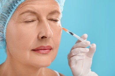 Doctor giving facial injection to senior woman on light blue background, closeup. Cosmetic surgery