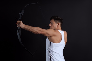 Photo of Man with bow and arrow practicing archery on black background