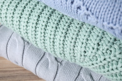 Stack of folded warm sweaters on wooden table, closeup