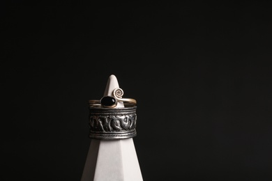 Photo of Stylish rings on stand against black background, space for text. Luxury jewelry