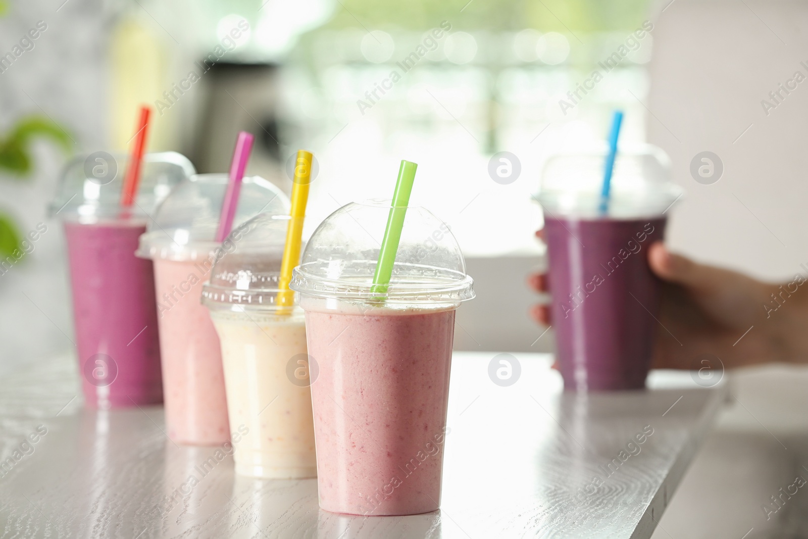 Photo of Different milk shakes in plastic cups on white wooden table indoors