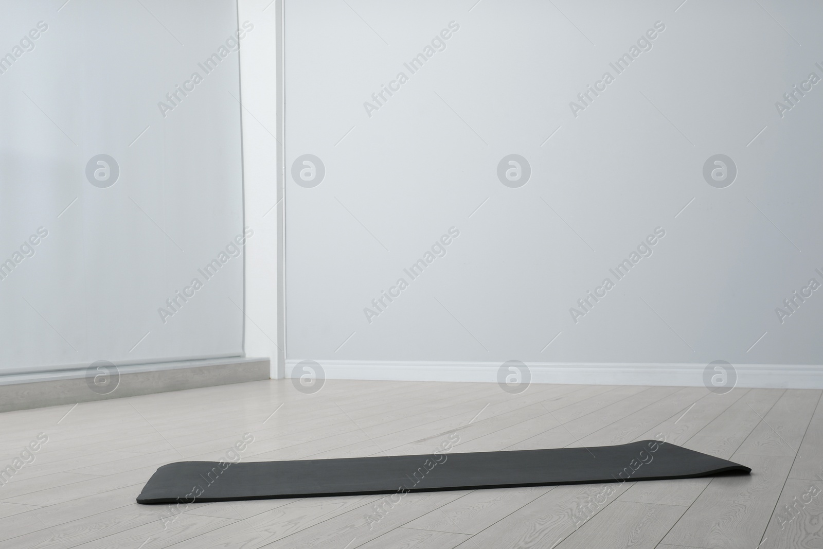 Photo of Unrolled black yoga mat on floor in room. Space for text